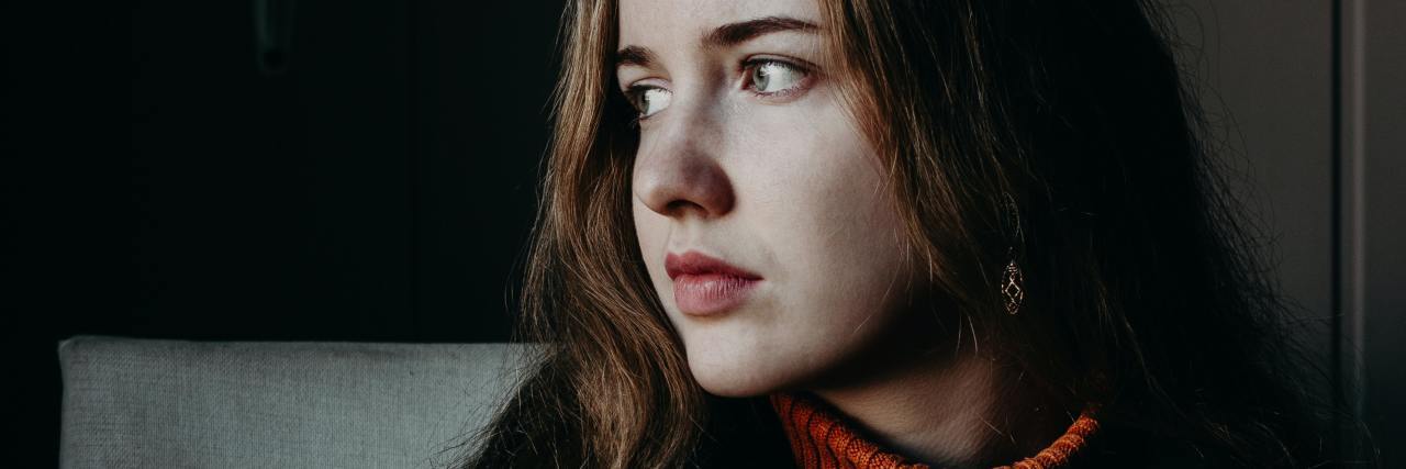 Dating Apps Are Triggering for Me After Sexual Trauma photo of young woman sitting at table with phone in hand, looking away from camera with concern or sadness
