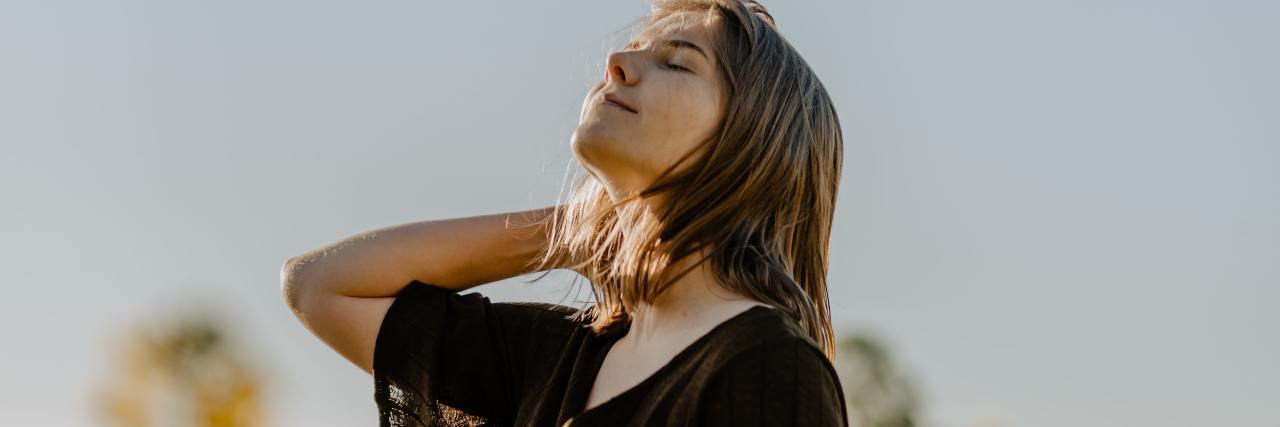 Read This If You Think Your Bipolar Disorder Is a Negative photo of woman with eyes closed and hand in hair, in the middle of a field of yellow flowers