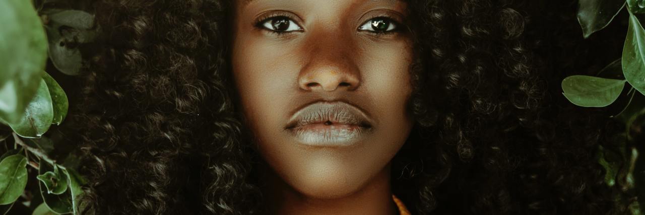 Struggle of Mental Illness and Being Black During Black Lives Matter photo of woman with leaves around her, looking into camera with serious expression