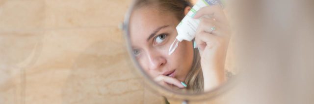 photo of woman's face reflected in mirror as she applies face cream