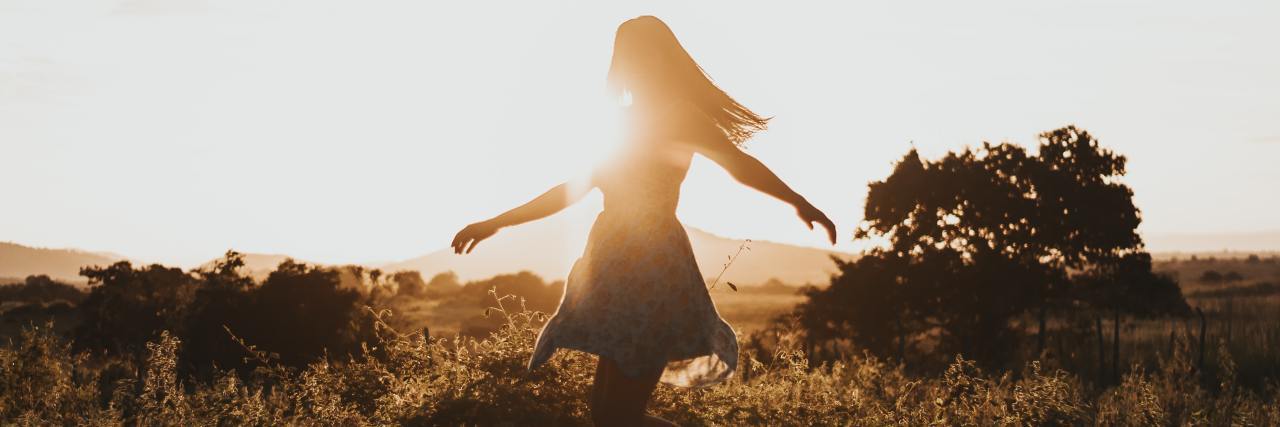 I Won't Hide My Old Mental Health Stories photo of young woman standing in a field, silhouetted by the sun