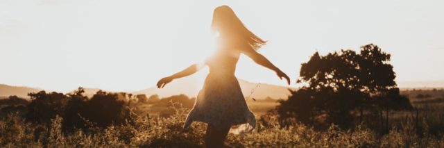 photo of young woman standing in a field, silhouetted by the sun