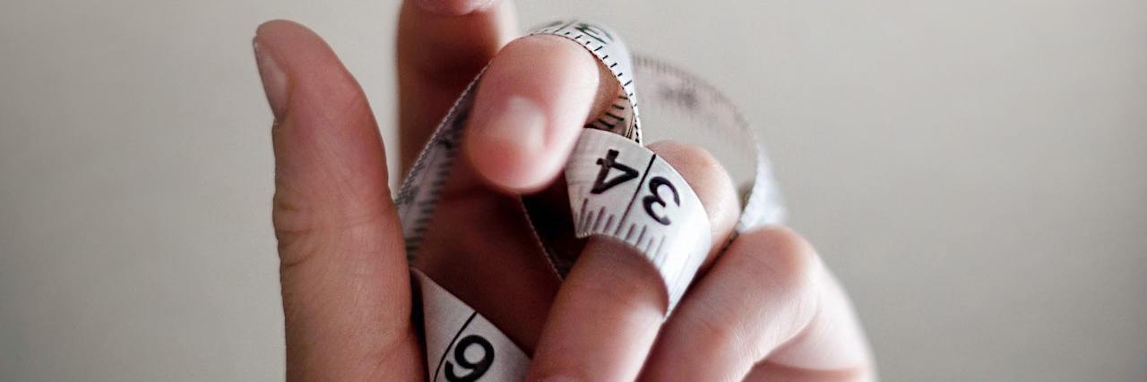 Living With an Eating Disorder and Worshiping Diet Culture A woman with a tape measurer around her fingers