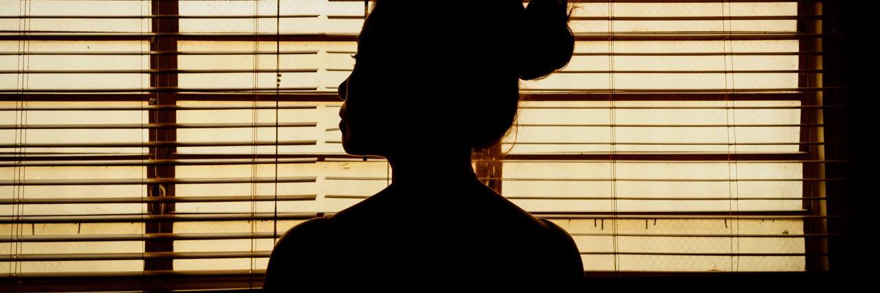 photo of woman silhouetted in front of window blinds