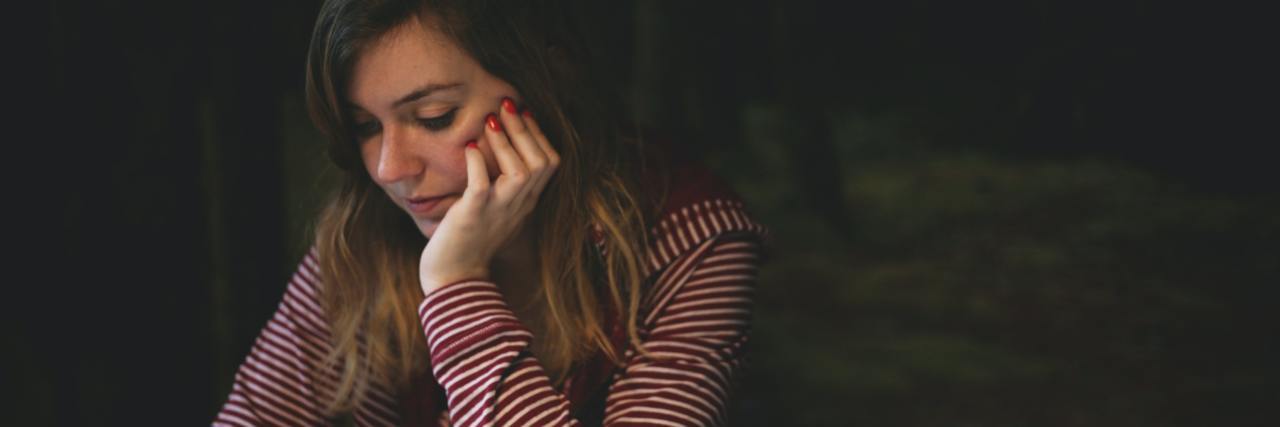 Undiagnosed Trauma Made Me Scared of Being Kissed in High School photo of young woman looking down, concerned, with her cellphone in her hand