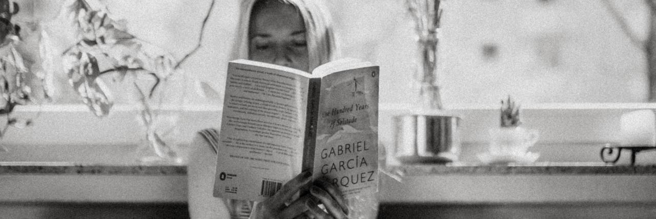 Dealing With UK COVID-19 Lockdown and Mental Health black and white photo of woman sitting on bed by window, reading a book