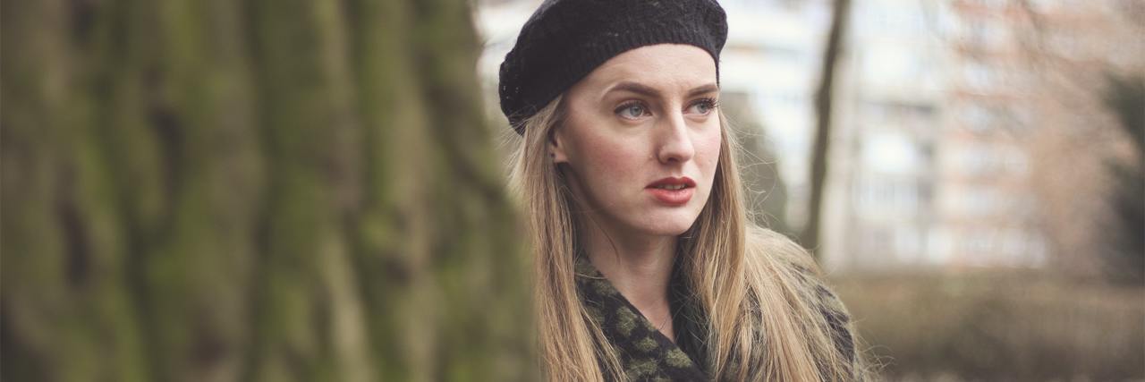 What It’s Like to Experience an ‘Unconventional’ Eating Disorder and Specific Phobia photo of woman wearing hat partially hidden behind a tree, looking away