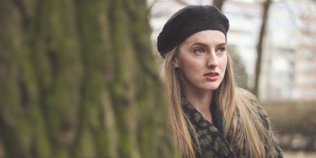 photo of woman wearing hat partially hidden behind a tree, looking away