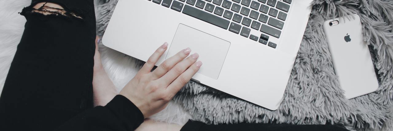 Could Computers Use Language Learning to Help Diagnose Mental Illness? photo of person crosslegged with ripped black jeans and laptop, taken overhead