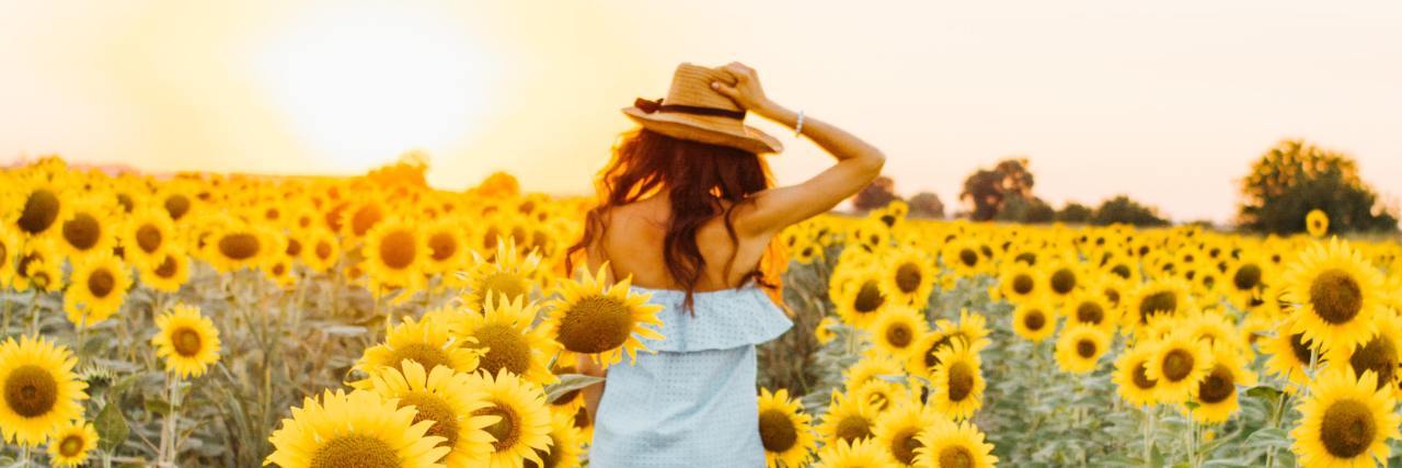 photo of woman walking through sunflower field at sunset