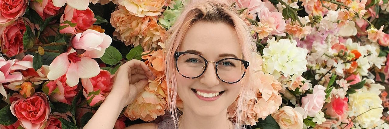 Smiling young woman with glasses, surrounded by flowers