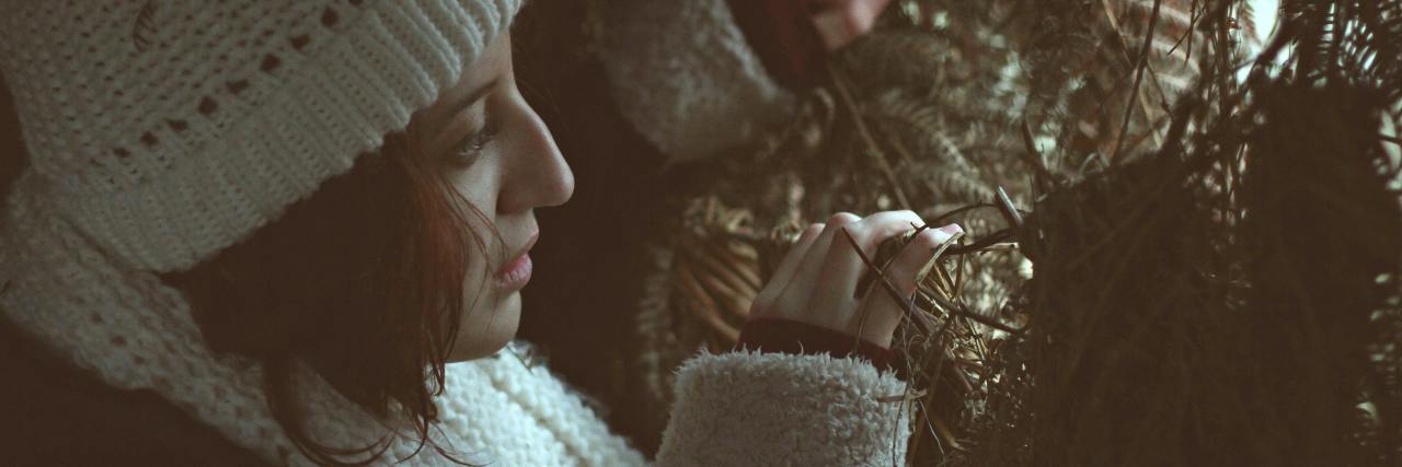 Feeling Like I Should Hide My Psychosis or Schizoaffective Disorder photo of woman wearing a hat and heavy coat, peeking through branches into the light