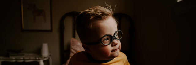 Boy with Down syndrome wearing a yellow shirt and glasses.