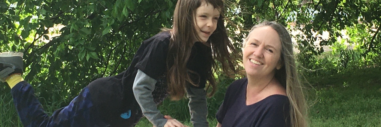 Self-Acceptance and Compassion in Pandemic Parenting A parent and child in nature, leaning on each other. Both have long hair and white skin.