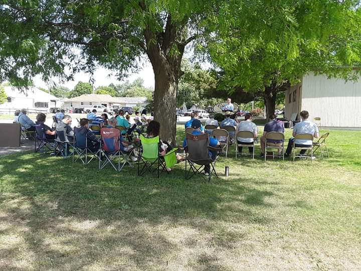 a group of people gathered outside for church, sitting in lawn chairs
