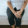 Woman sitting on bed and holding her knee