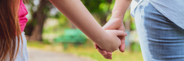 close up of a mom and daughter holding hands at park