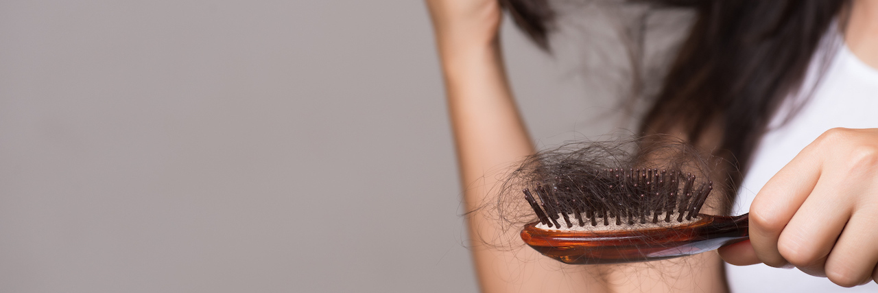 Woman with long brown hair holds a brush out to show hair loss