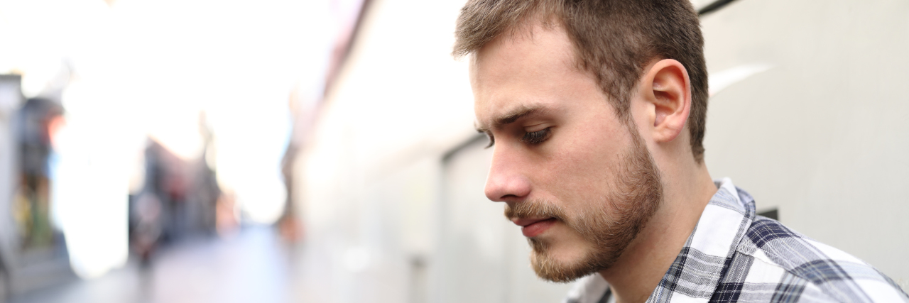 Feeling Isolated as a Young Person With Chronic Illness Sad man standing by a wall outside.