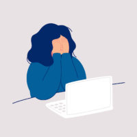 A woman covering her face with her hands in front of a computer