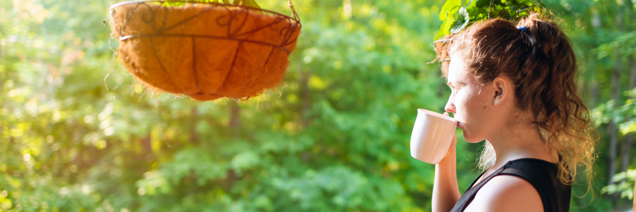 Defining Realistic Goals in Life With a Chronic Illness Woman standing on porch of house drinking tea or coffee.