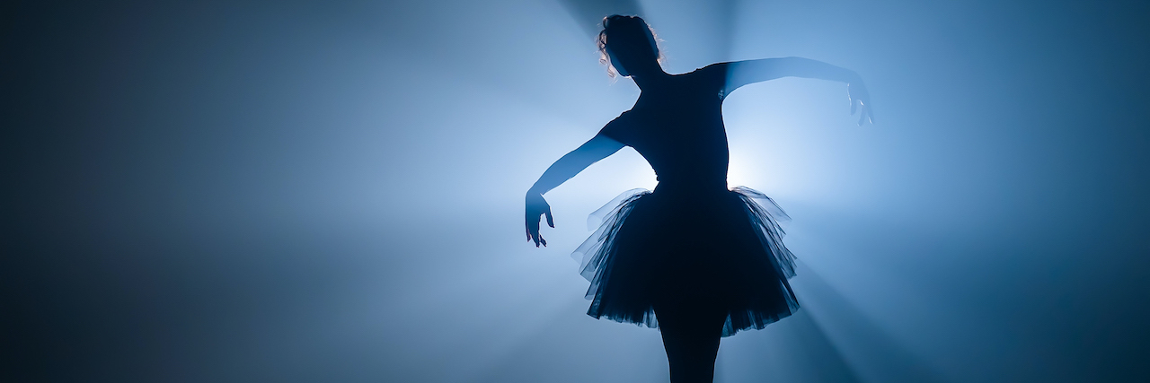 Ballerina in black tutu dress dancing on stage with magic blue light and smoke