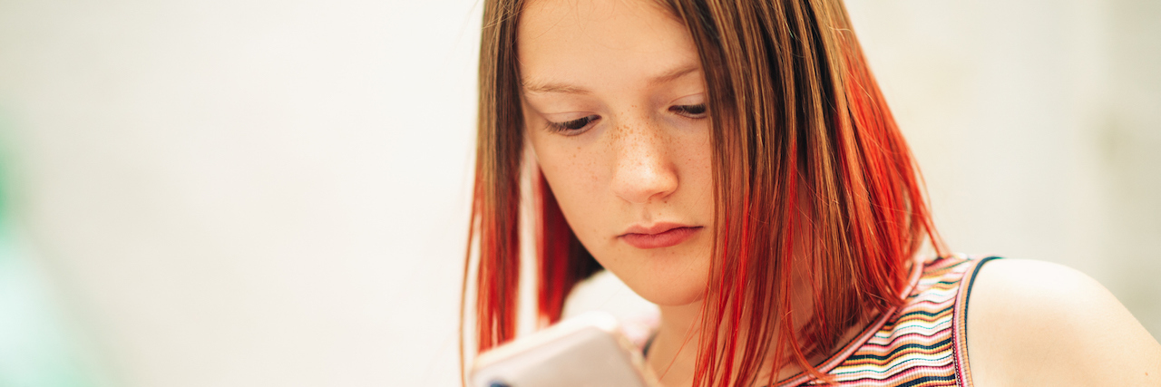 A teenager with died red hair on her smart phone