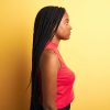 Profile of a black woman with long black hair. She's wearing a red shirt against a yellow background