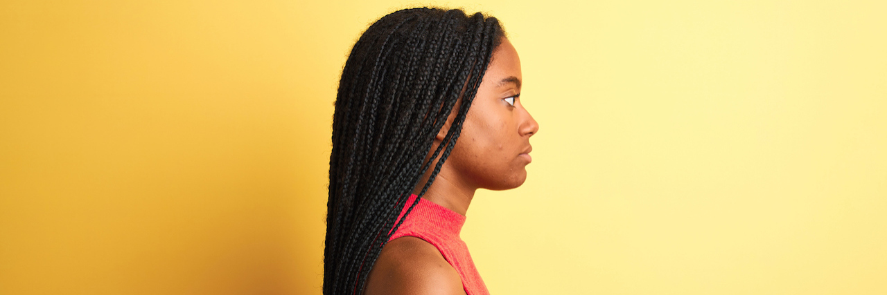 Profile of a black woman with long black hair. She's wearing a red shirt against a yellow background