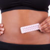 Woman hold contraception pills in front of her belly button