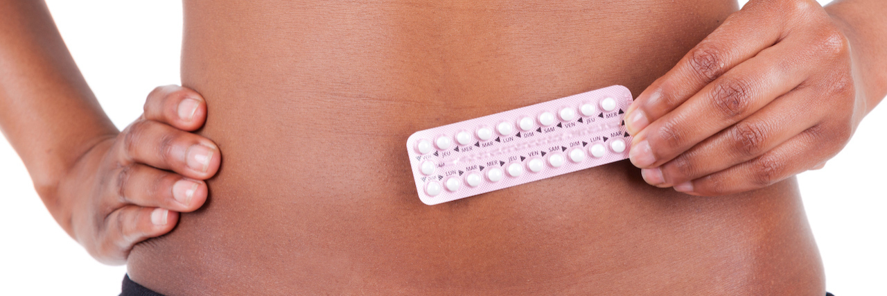 Woman hold contraception pills in front of her belly button