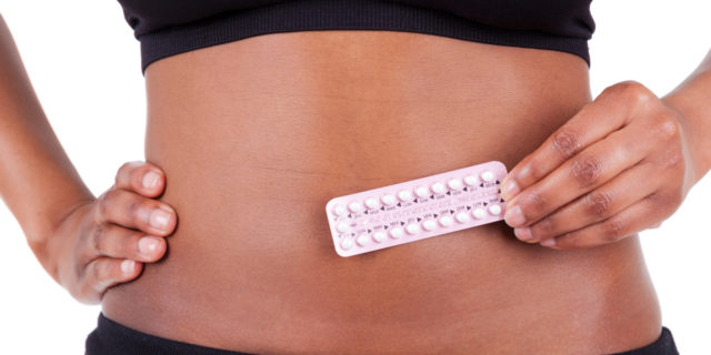 Woman hold contraception pills in front of her belly button