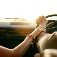 A woman holding her husband's hand in the car, his hands are on the wheel