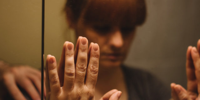 Sad woman looking in mirror.