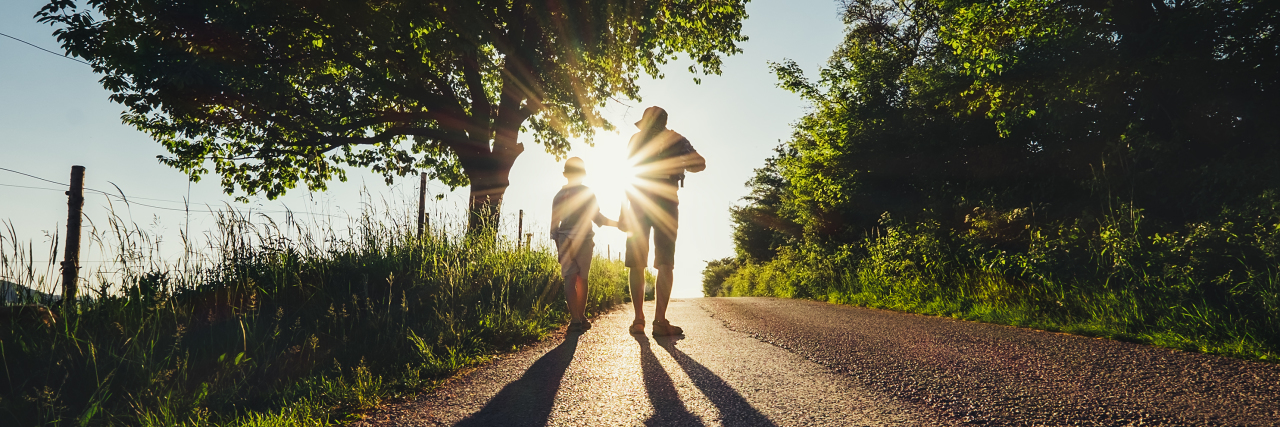 How I Feel About Leg Braces as a Dad of a Son With a Disability A father and a son walking together on a road during sunset