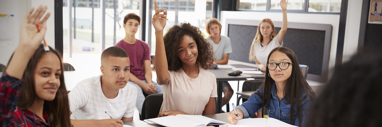 Diverse group of high school students raising hands in class