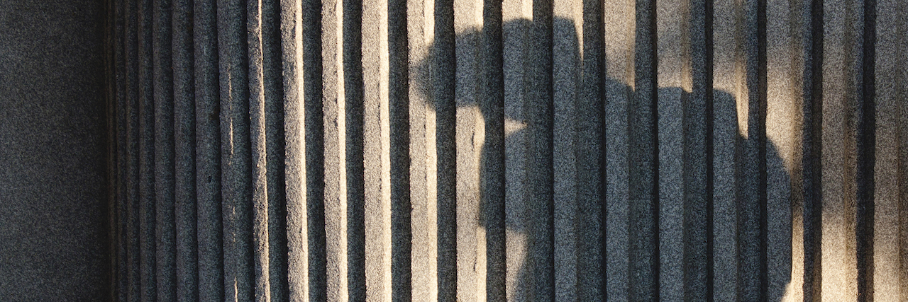 shadow of a boy with backpack against a ribbed concrete wall