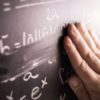 A hand wiping off a math equation written in chalk on a chalk board