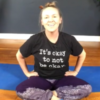 White woman sitting on the floor smiling in a t-shirt that says "It's okay to no be okay."