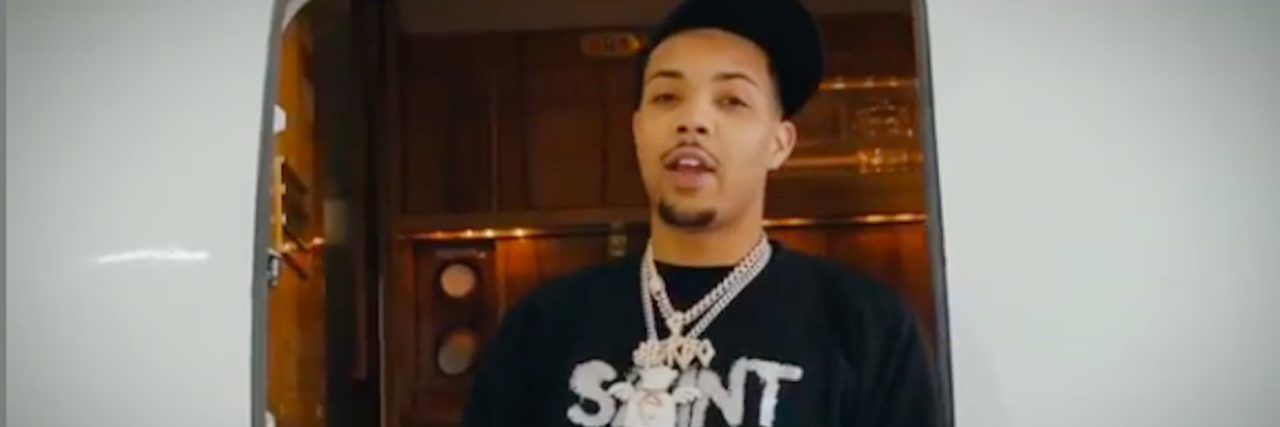 Rapper G Herbo wearing a black shirt, black cap and several chains standing in front of an open airplane door