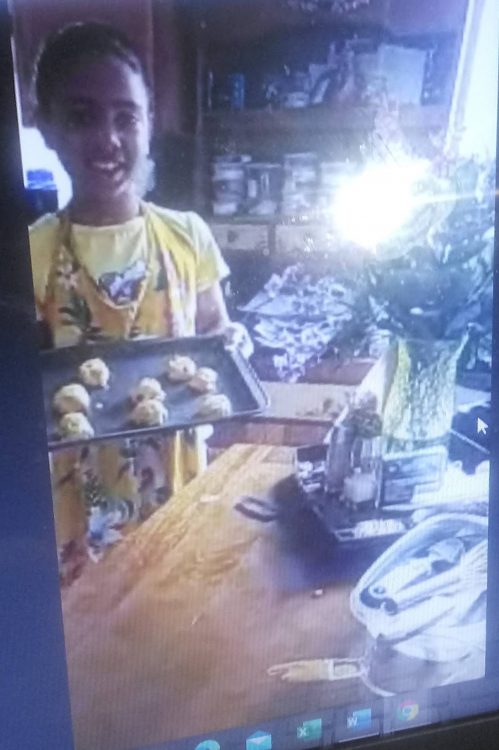 A young girl holding up cookies over a screen