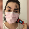 A woman wearing a pink mask, with a Pulse Oximeter on her finger