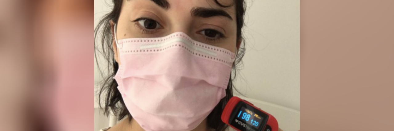 Masks Are Not a Health Risk, Just Ask Chronically Ill People A woman wearing a pink mask, with a Pulse Oximeter on her finger