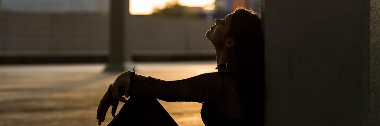 photo of woman sitting on a roof at sunset looking upset, with her head resting back against a wall