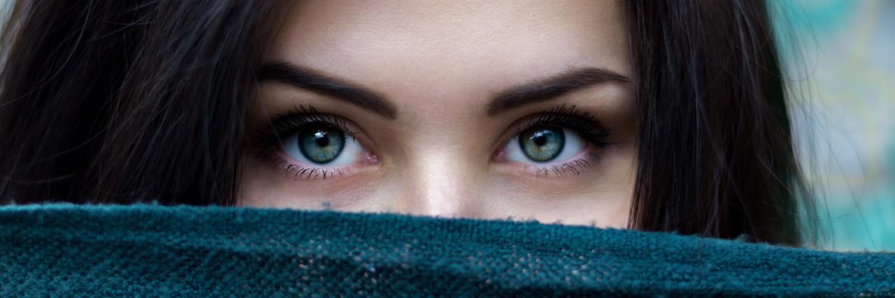 A woman looking from behind a blanket, all you can see are her eyes up