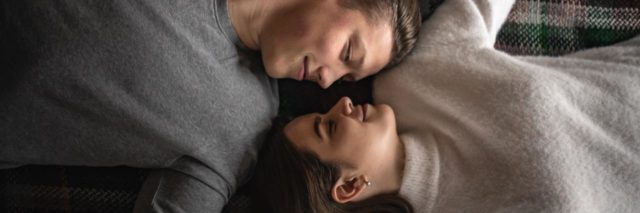 overhead photo of couple lying together in opposite directions and looking into each others' eyes