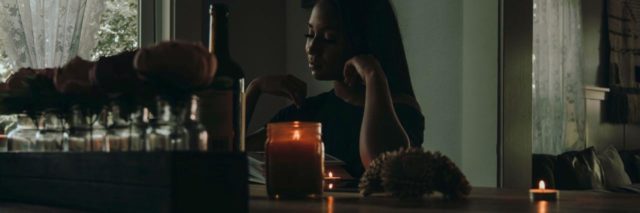 photo of Black woman sitting at a wooden counter, a candle nearby