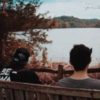 photo of two men sitting by lake and talking