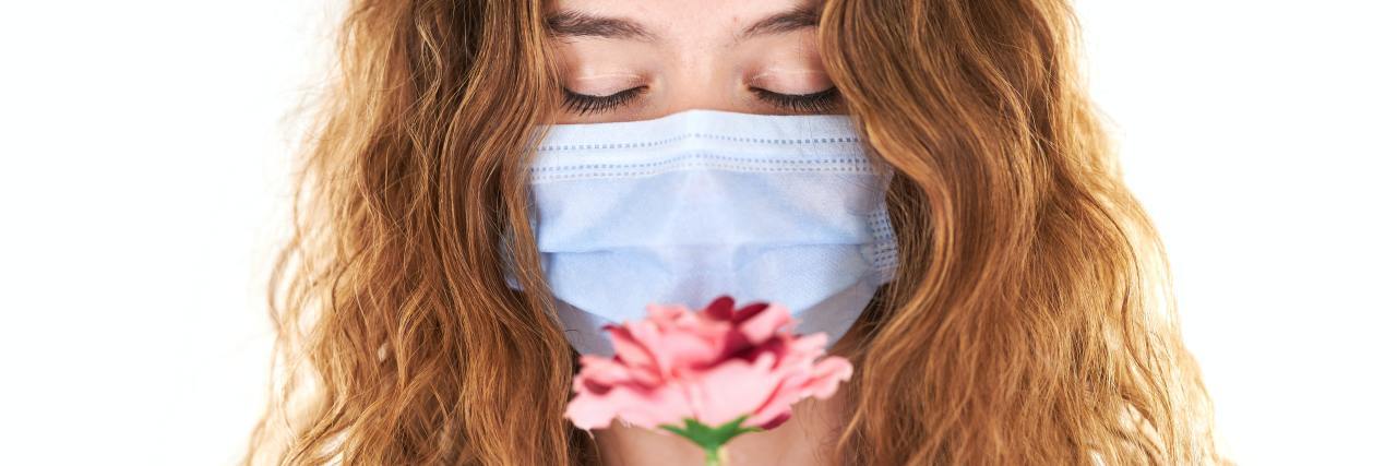 How Empathy Will Help Us Prevent the Worst Outcome of COVID-19 photo of woman wearing a face mask and looking down at a pink flower she is holding in her hands