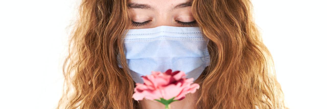 photo of woman wearing a face mask and looking down at a pink flower she is holding in her hands